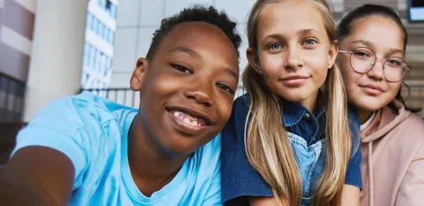 Three kids smile while looking at a camera.