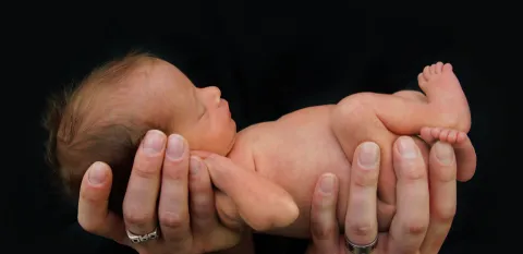 Parent caring for a preemie and holding the baby in their hands against a black background
