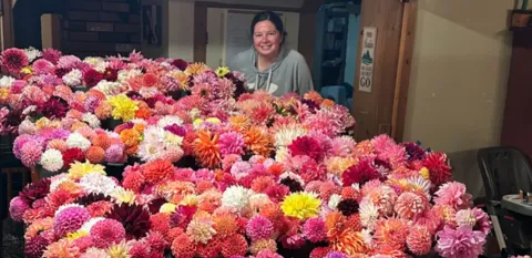 Sarah Skinner stands behind a table covered in dahlias of all different colors.