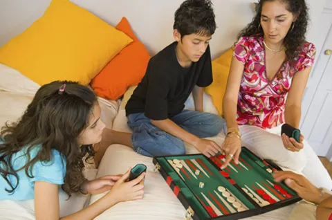 Mom and 2 kids playing backgammon spending screen free time as a family