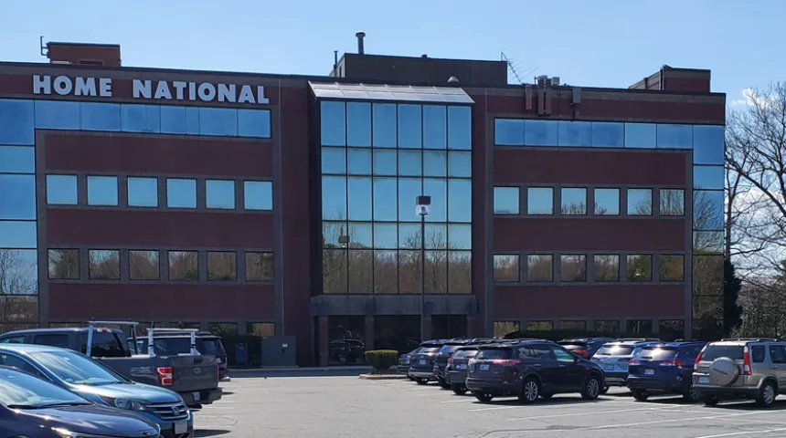 The exterior of a brick building. Many cars are in the parking lot. A sign outside the building reads "Home National."