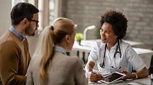 A doctor meets with a couple and analyzes their medical test results on digital tablet during an appointment.