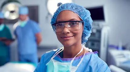 A CRNA who's part of the Anesthesia Team looks up from her work in the Operating Room and gives a smile.