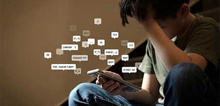 A boy sits on the stairs, looking at his phone and showing signs of distress.