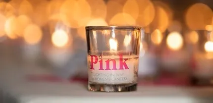 A candle that says "pink" sitting in front of several other lit candles.