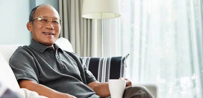 Smiling senior man sitting with a warm drink in his his home, as he looks toward the camera.