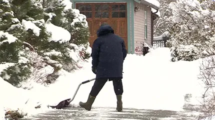 A person shovels a driveway - their back is to the camera.