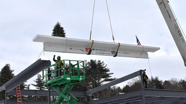 Construction workers on top of a large slab being hoisted onto the frame of the Nashoba emergency facility.