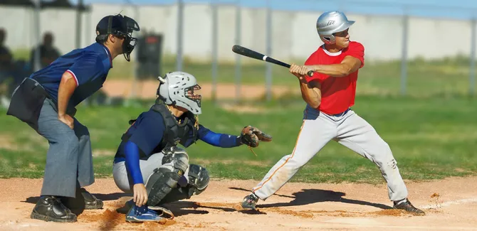 A batter is ready to swing at home plate with the umpire and catcher ready to participate in the play.