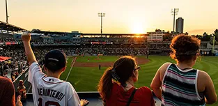 The sun sets behind Polar Park in Worcester as young WooSox fans watch the team play baseball.