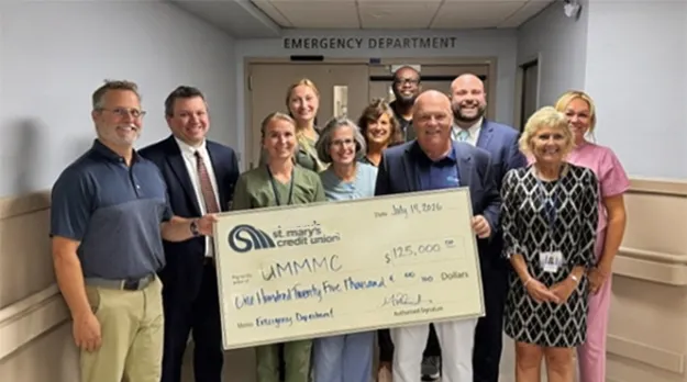 UMass Memorial Health staff stand in front of the interior doors to the Emergency Department and hold a banner of a check from St. Mary's Credit Union for $125,00.0