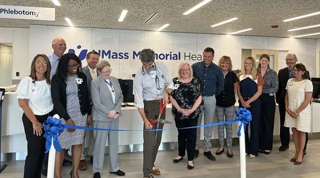 A diverse group of people watch as the ribbon is cut in the entrance to the new Family Medicine at White City Plaza.