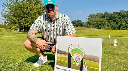 Ryan Horgan poses on a golf course with a sign for his father's golf tournament 