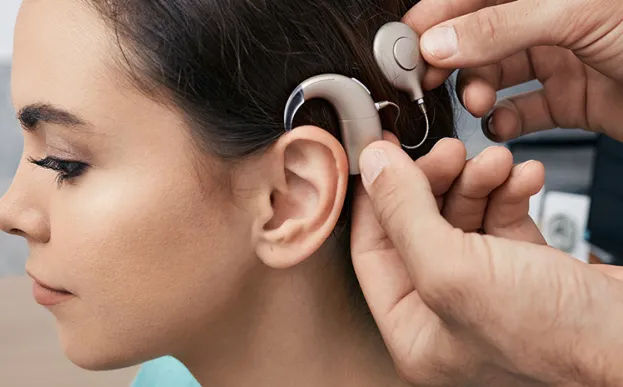 Having recovered from the cochlear implant surgery, a young female patient has her sound processor fitted behind her ear.