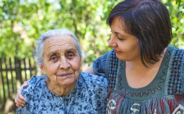 Loving daughter puts arm around elderly mother as she avoids caregiver burnout