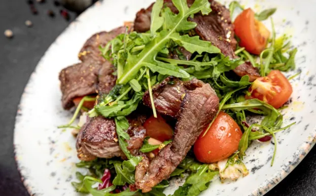 New York strip steak salad with steak on a bed of lettuce on a white plate