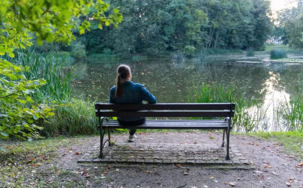 woman sitting on bench looking at trees and pond practicing mindfulness in nature