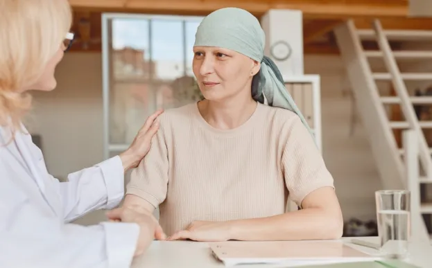Woman with cancer wearing head cover is comforted by an oncology nurse navigator