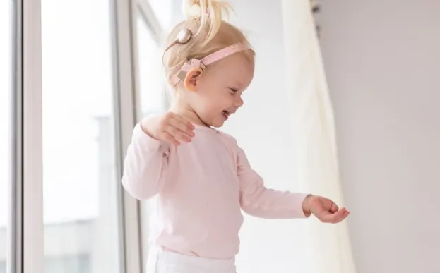 Toddler girl with cochlear implant smiling as she is discovering the world around her