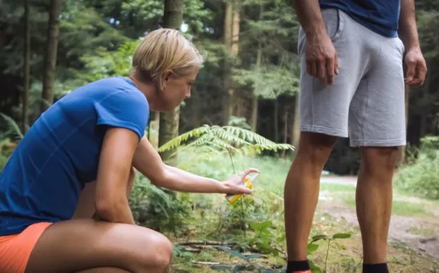Woman bending down putting bug spray on a man's legs while hiking in the woods.