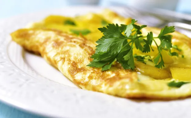 Omelet stuffed with potato and vegetables on a white plate on blue wooden background