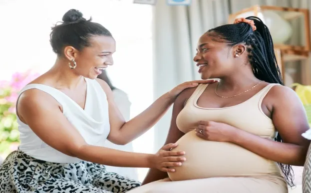 A black pregnant woman talking and smiling with her doula on a couch