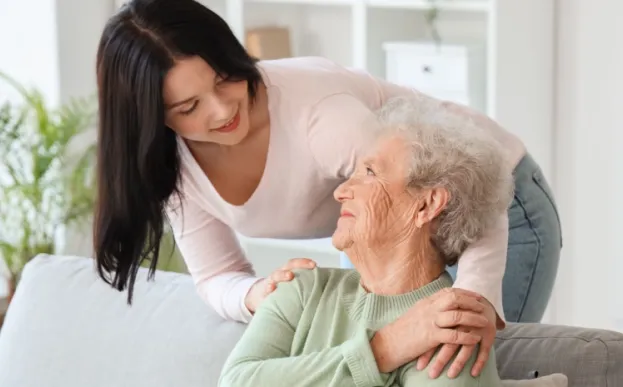 daughter standing behind a couch hugging grandmother while ensuring she is in a safe home