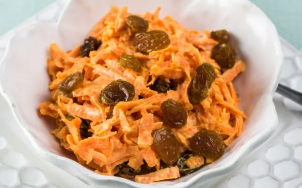 carrot and raisin slaw in a white serving bowl