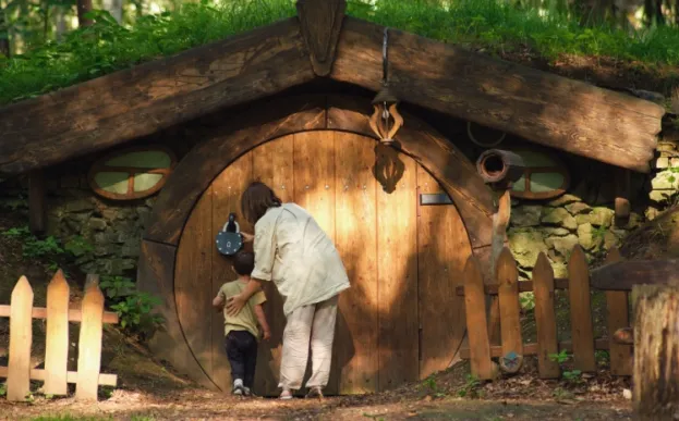 child and adult looking at a hobbit house in the woods.