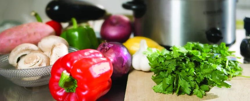 Various vegetables are shown on a cutting board in front of a crock-pot.