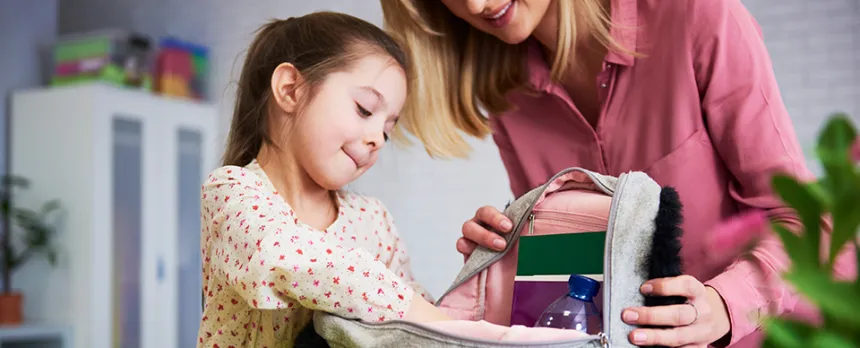 mom helping daughter pack backpack for school