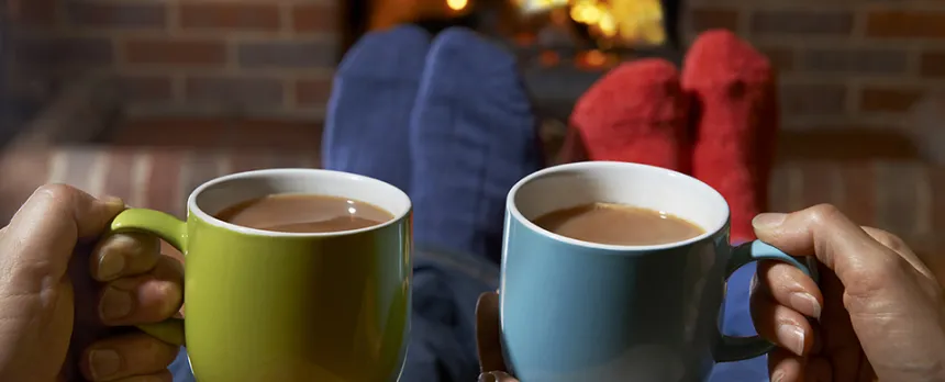 two people drinking hot chocolate by the fireplace