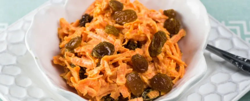 carrot and raisin slaw in a white serving bowl