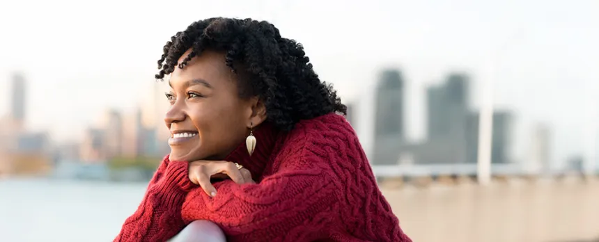 happy woman looking at a river with a city skyline in the background