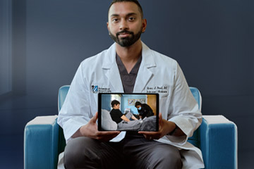 A UMass Memorial Health physician holds a tablet displaying his video connection with a patient