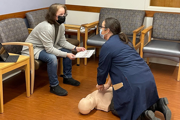 A woman takes direction from another while performing chest compressions on a CPR mannequin.