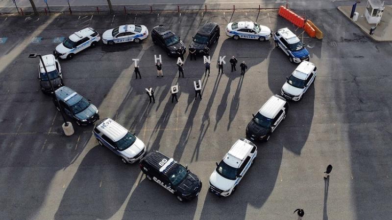Cars are organized in the shape of a heart with people holding signs that read 'Thank You'.